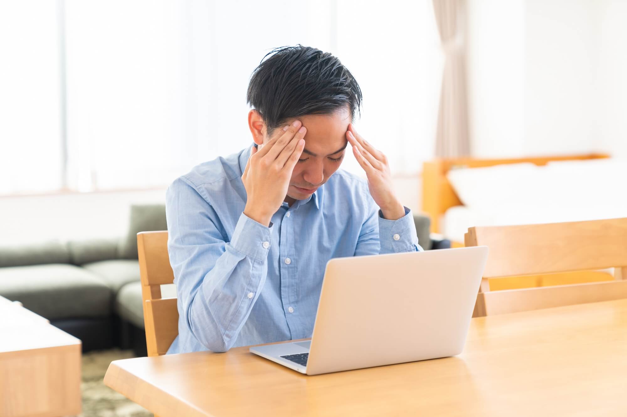 ノートPCの前で頭を抱えて悩んでいる男性